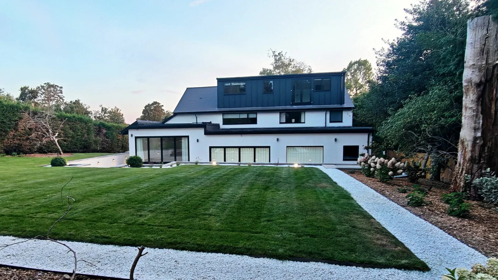 The same Cobham house after, white render, a new roof storey and a striped lawn