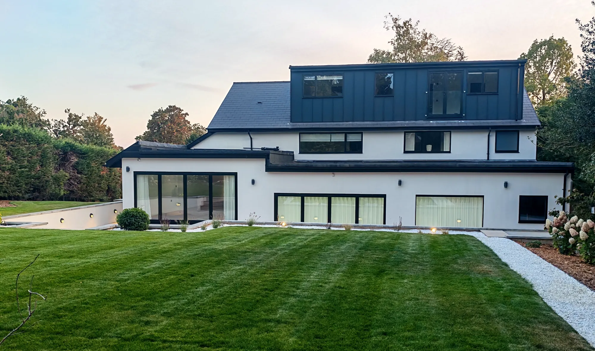 White modern family home in Cobham after a full refurbishment, at dusk across a striped lawn