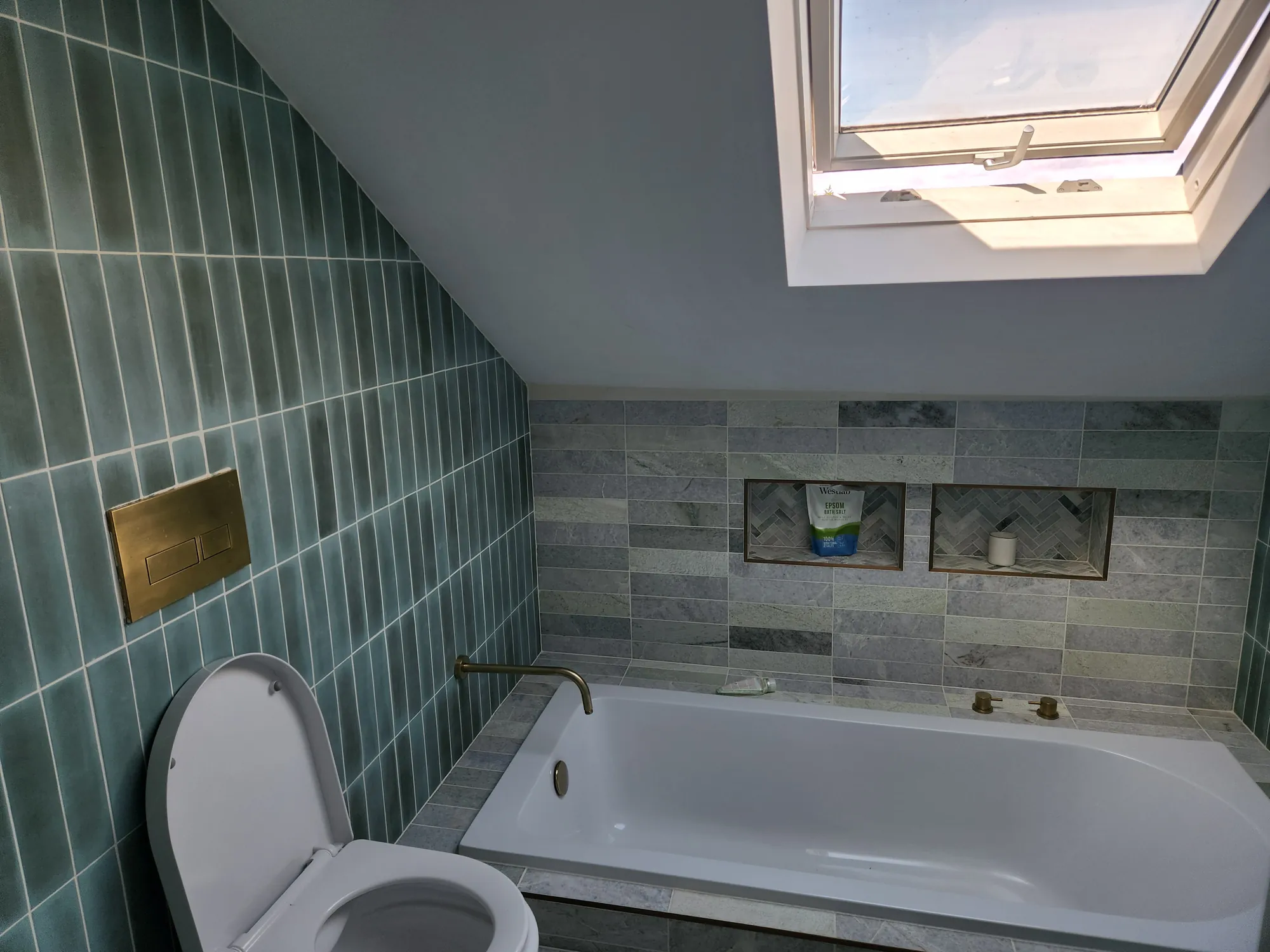 Loft bathroom with green tiling under the roof window